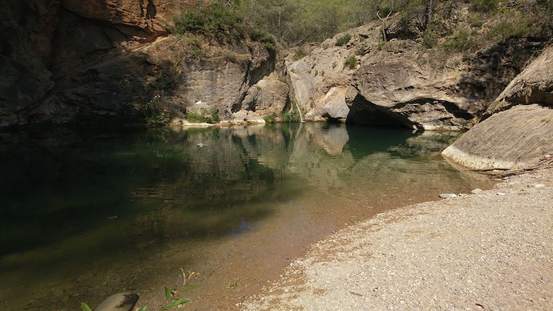 El espectacular Pozo Negro de Ludiente Vista panorámica del Pozo Negro de Ludiente, una gran poza de aguas turquesa rodeada de imponentes paredes de roca.